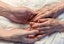 A younger persons hand gently holding an elderly persons hand on a quilted surface