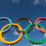 Five interlocking Olympic rings against a blue sky with clouds