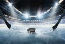 Close-up of a hockey puck on the ice with a hockey stick in the foreground