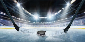 Close-up of a hockey puck on the ice with a hockey stick in the foreground