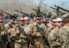 Group of military personnel in camouflage uniforms standing with weapons during a training exercise