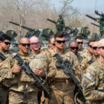 Group of military personnel in camouflage uniforms standing with weapons during a training exercise