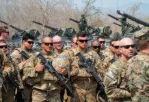 Group of military personnel in camouflage uniforms standing with weapons during a training exercise