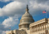 The U.S. Capitol building with a dome and an American flag under a cloudy sky