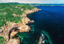 Aerial view of rocky cliffs meeting the ocean with lush green hills in the background