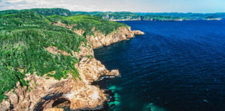 Aerial view of rocky cliffs meeting the ocean with lush green hills in the background
