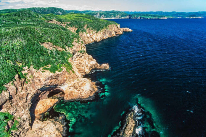 Aerial view of rocky cliffs meeting the ocean with lush green hills in the background