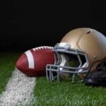 A football helmet, a football, and cleats on a field