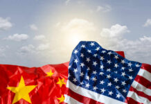Crumpled flags of the United States and China against a cloudy sky