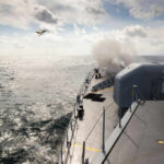 Naval ship firing a cannon with a fighter jet flying overhead