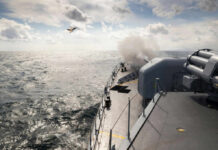 Naval ship firing a cannon with a fighter jet flying overhead