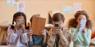 Four children sitting together, each focused on their electronic devices