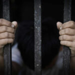 A childs hands gripping prison bars, conveying a sense of confinement and distress