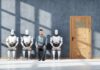 A man sitting between three humanoid robots in a waiting room for a job interview