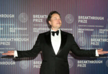 A man in a tuxedo posing at an award ceremony backdrop