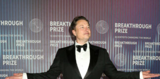 A man in a tuxedo posing at an award ceremony backdrop