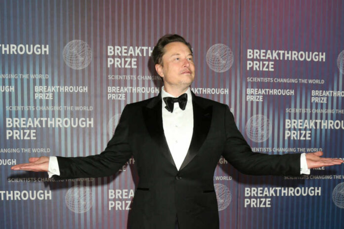 A man in a tuxedo posing at an award ceremony backdrop