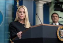 A woman at a podium during a press conference with a man in the background