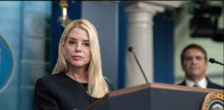 A woman at a podium during a press conference with a man in the background