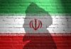 Iran’s Leader “Missing” After SHOCKING Hospitalization Silhouette of a figure against the Iranian flag painted on a brick wall