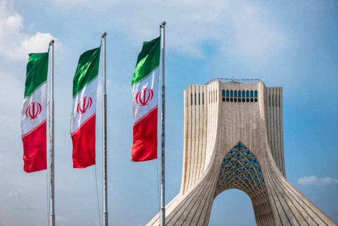 Three Iranian flags in front of the Azadi Tower against a blue sky