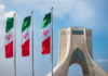 Three Iranian flags in front of the Azadi Tower against a blue sky