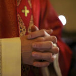 Pope Leo’s Bold Move Stuns Vatican A close-up of a priests hands clasped together, wearing red vestments