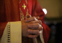 Pope Leo’s Bold Move Stuns Vatican A close-up of a priests hands clasped together, wearing red vestments