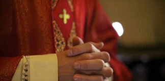 A close-up of a priests hands clasped together, wearing red vestments
