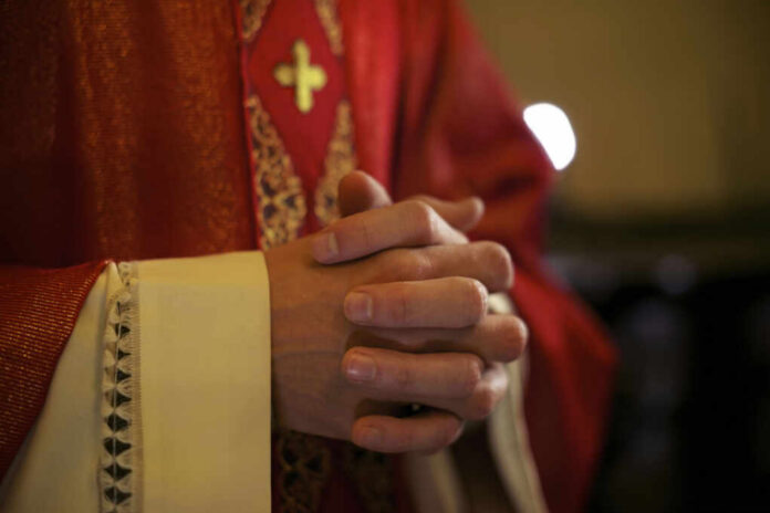 A close-up of a priests hands clasped together, wearing red vestments