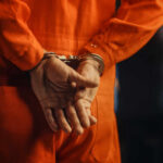 Individual in an orange jumpsuit with hands cuffed behind their back