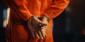 Individual in an orange jumpsuit with hands cuffed behind their back