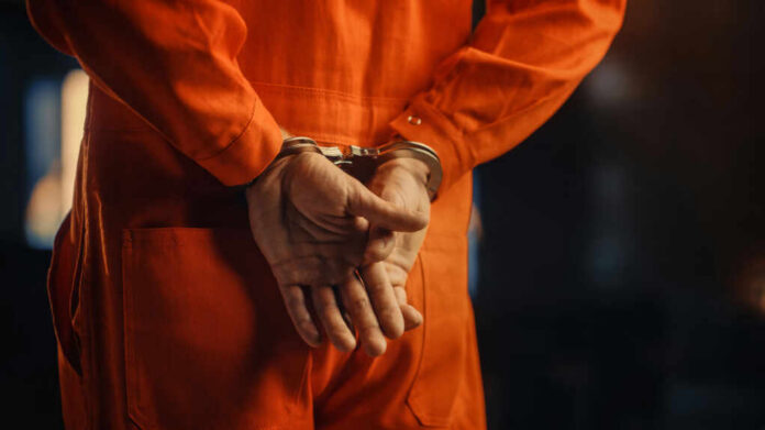Individual in an orange jumpsuit with hands cuffed behind their back