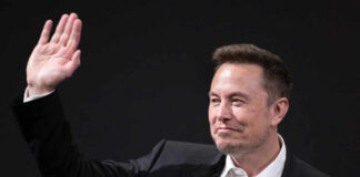 A man in a suit waving with a smile during a conference