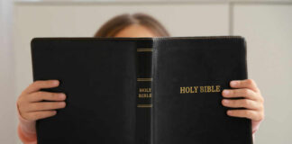 Child holding a black Holy Bible in front of their face
