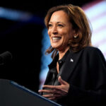 A woman smiling while speaking at a podium with a microphone