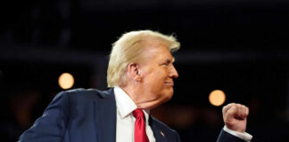 A man in a suit making a celebratory gesture during a speech