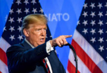 Trump’s Iran Threat Sparks UK Fury A man delivering a speech with American flags in the background