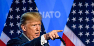 A man delivering a speech with American flags in the background