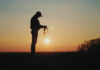 Silhouette of a farmer holding soil against a sunset backdrop