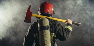 Firefighter in protective gear holding an axe against a smoky background