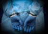 Hands in blue gloves handcuffed together, wearing medical attire