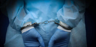 Hands in blue gloves handcuffed together, wearing medical attire