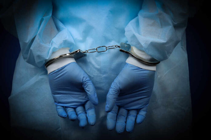 Hands in blue gloves handcuffed together, wearing medical attire