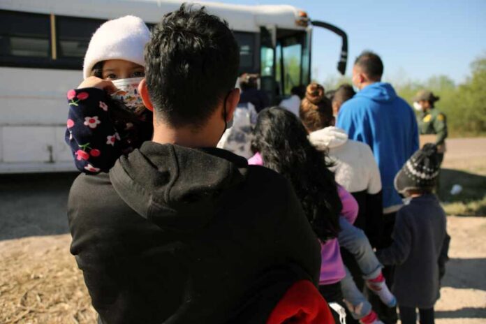 A parent holding a child in line near a bus with other individuals waiting