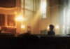 A solitary figure sitting in a church with soft lighting and candles