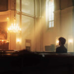 A solitary figure sitting in a church with soft lighting and candles