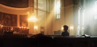 A solitary figure sitting in a church with soft lighting and candles