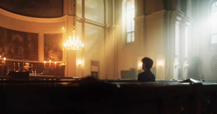 A solitary figure sitting in a church with soft lighting and candles