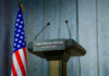 Press podium with microphones and American flag in the background